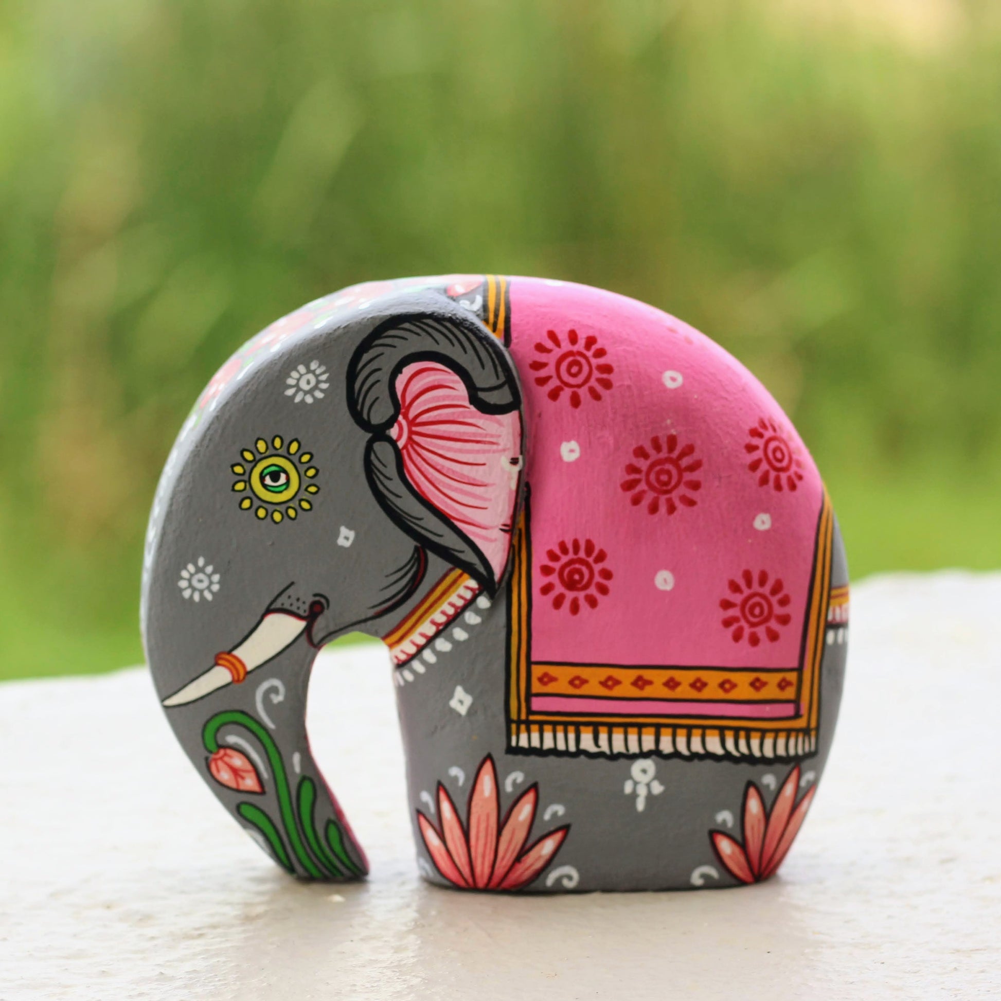 Decorative elephant figurine with pink and gray design on a blurred green background